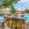 a backyard with a pool and a brick patio with a tree and houses in the background